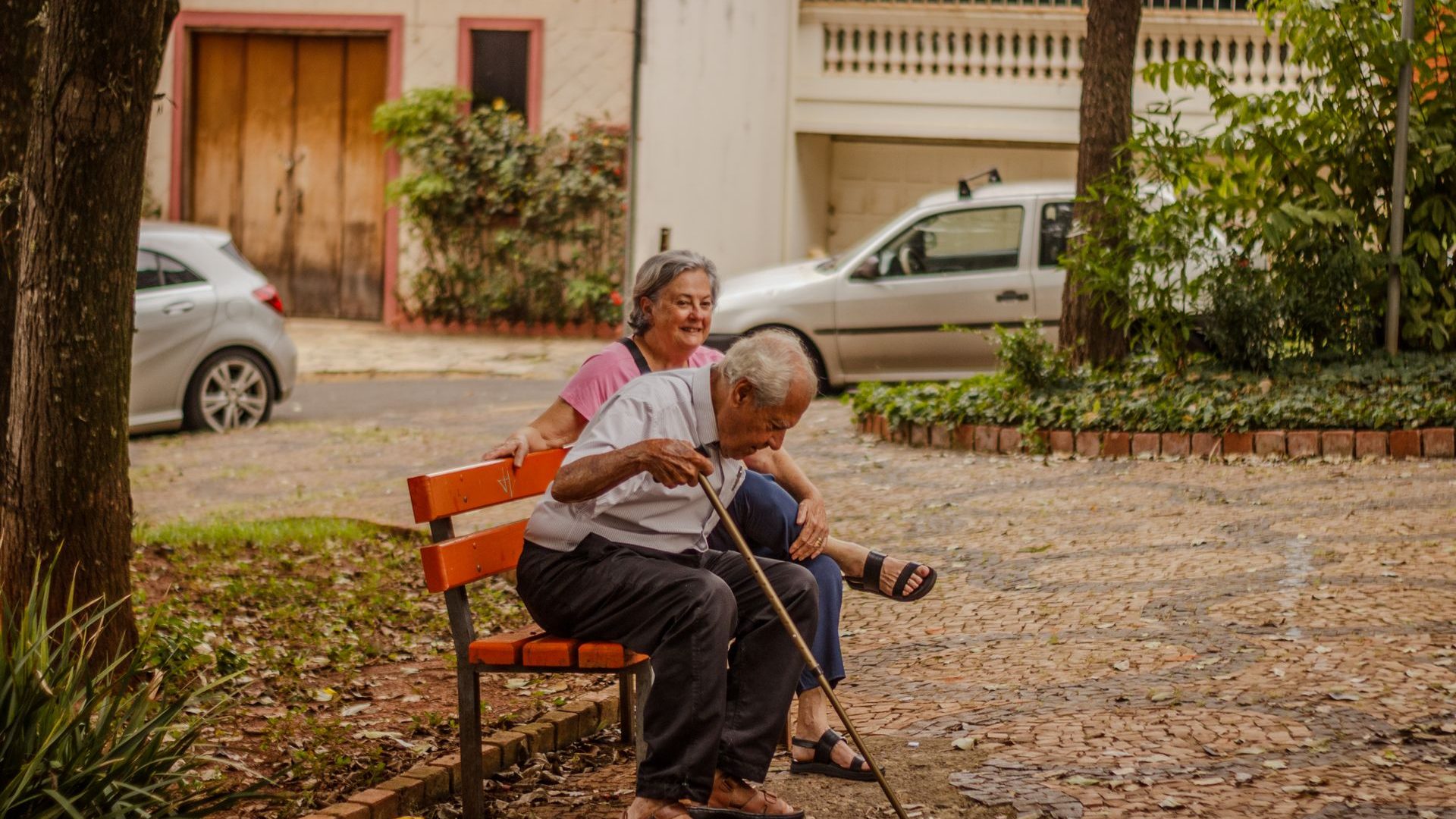Casal idoso sentado em um banco de praça numa cidade do interior
